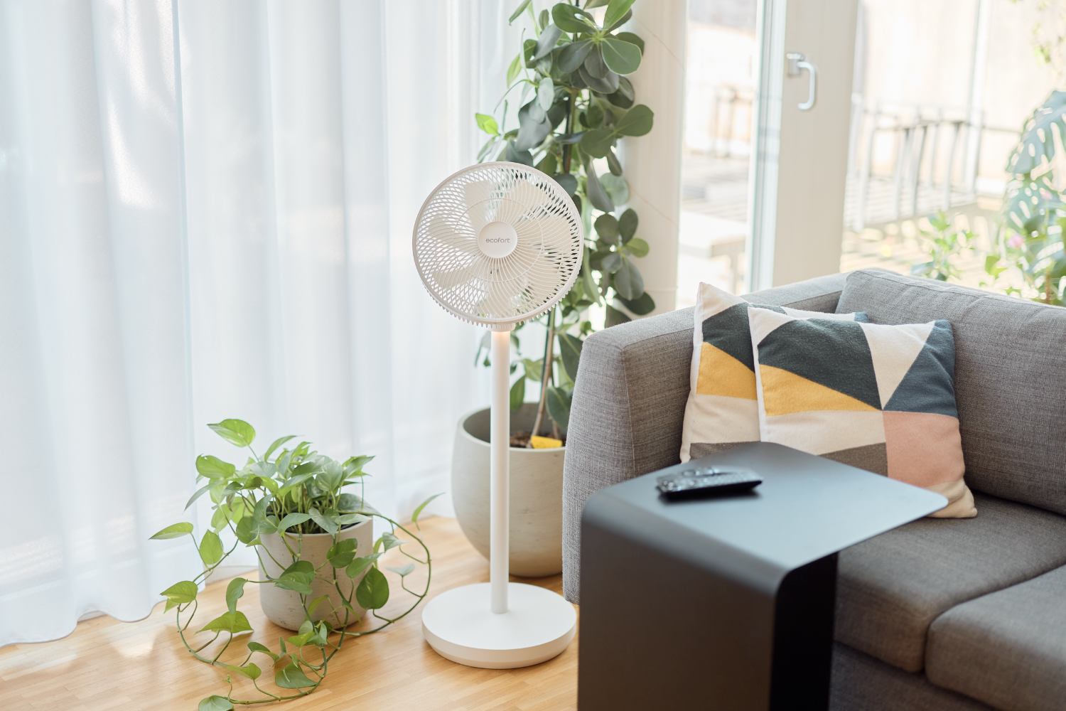 Ventilateur ecoQ SilenAir Due+ à côté d'un canapé et de plantes d'intérieur dans un salon moderne et confortable.